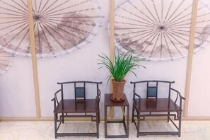 Two wooden chairs with a potted plant between them, against a wall with circular wall decorations. - Liyang Nanshan Zhuhai Cuigu Manor Hotel (Liyang)