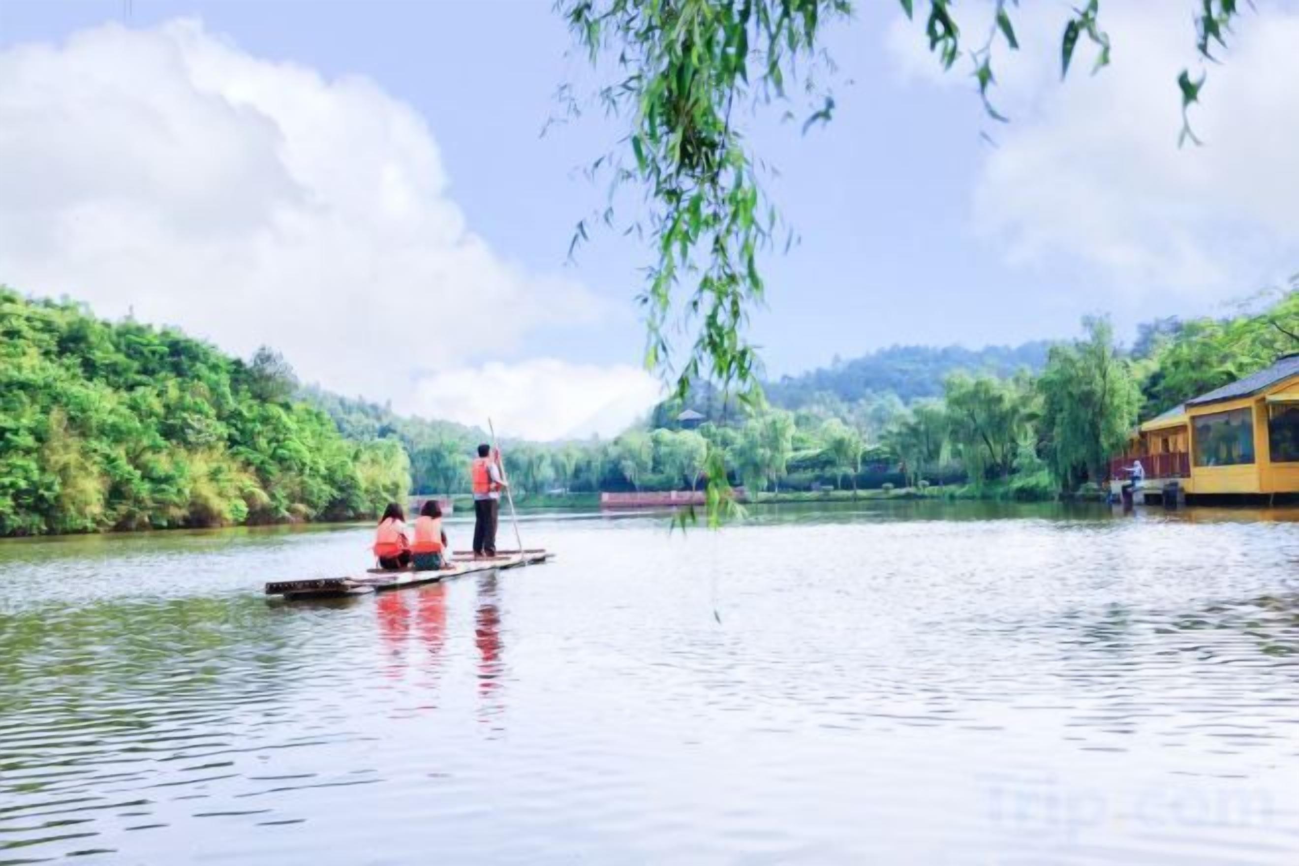 A calm river with a boat carrying people, surrounded by lush greenery and a building on the right.
