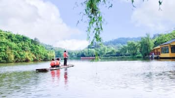 A calm river with a boat carrying people, surrounded by lush greenery and a building on the right.