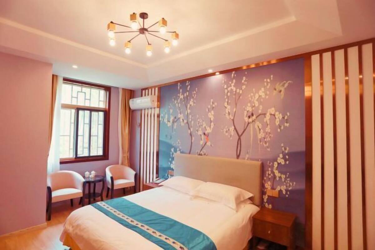 A bedroom with a bed, a chandelier, a window, and a wall with a floral design.