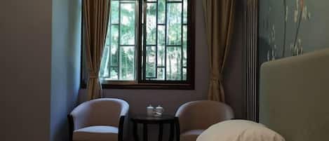 A hotel room with a bed, two chairs, a small table with a teapot and cup, and a window with curtains.