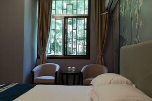 Habitación de hotel con cama, dos sillas, una mesita con tetera y taza, y una ventana con cortinas.