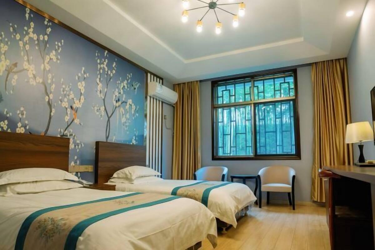 A hotel room with two beds, a desk, a chair, a window with curtains, and a ceiling light fixture.