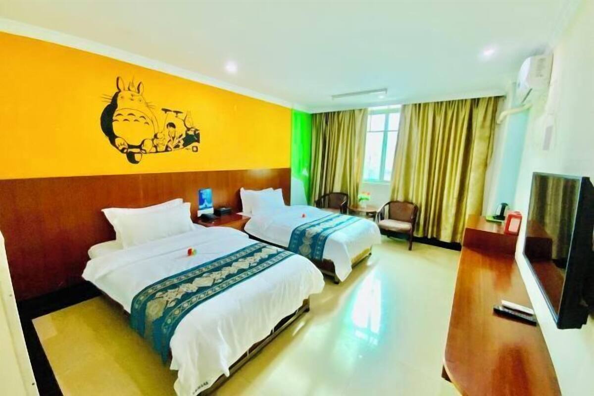 A hotel room with two beds, a television, a desk, and a wall mural.