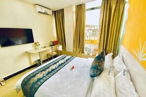 Een hotelkamer met een bed, een televisie, een klein bureau en een raam met gordijnen.