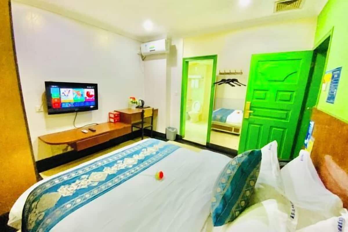A hotel room with a bed, a TV, a desk, and a green door.