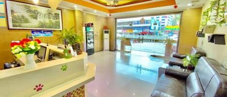 A hotel reception area with a reception desk, seating area, and a view of the street outside.