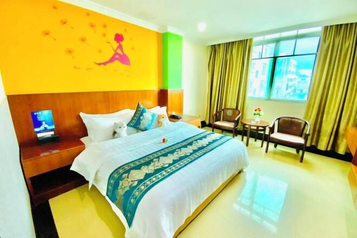 A hotel room with a bed, a desk with a computer, a chair, a small table, and a window with curtains.