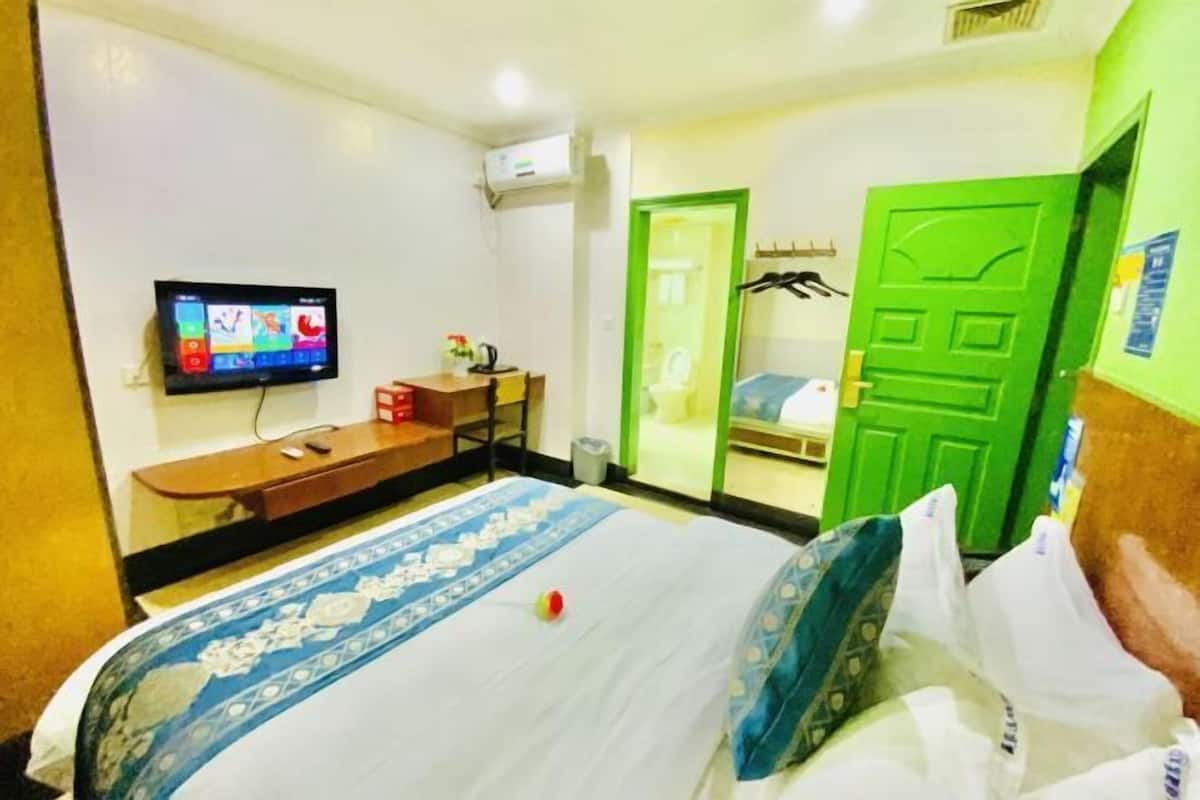 A hotel room with a bed, a TV, a desk, and a green door.