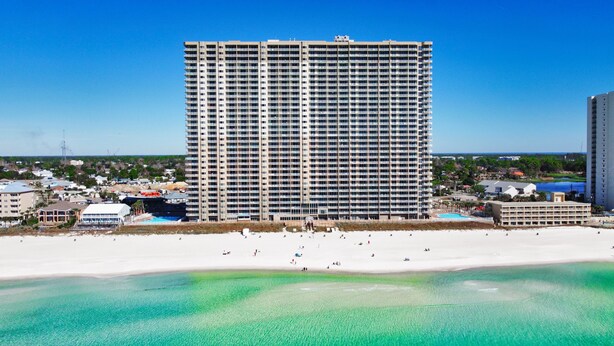 Un hotel de altura con varios pisos, una playa en primer plano y un cielo azul despejado.