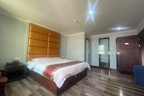 A hotel room with a large bed, a wooden headboard, a desk with a chair, and a door.