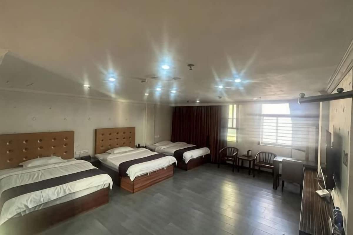 A hotel room with three beds, a desk, a chair, and a large window.