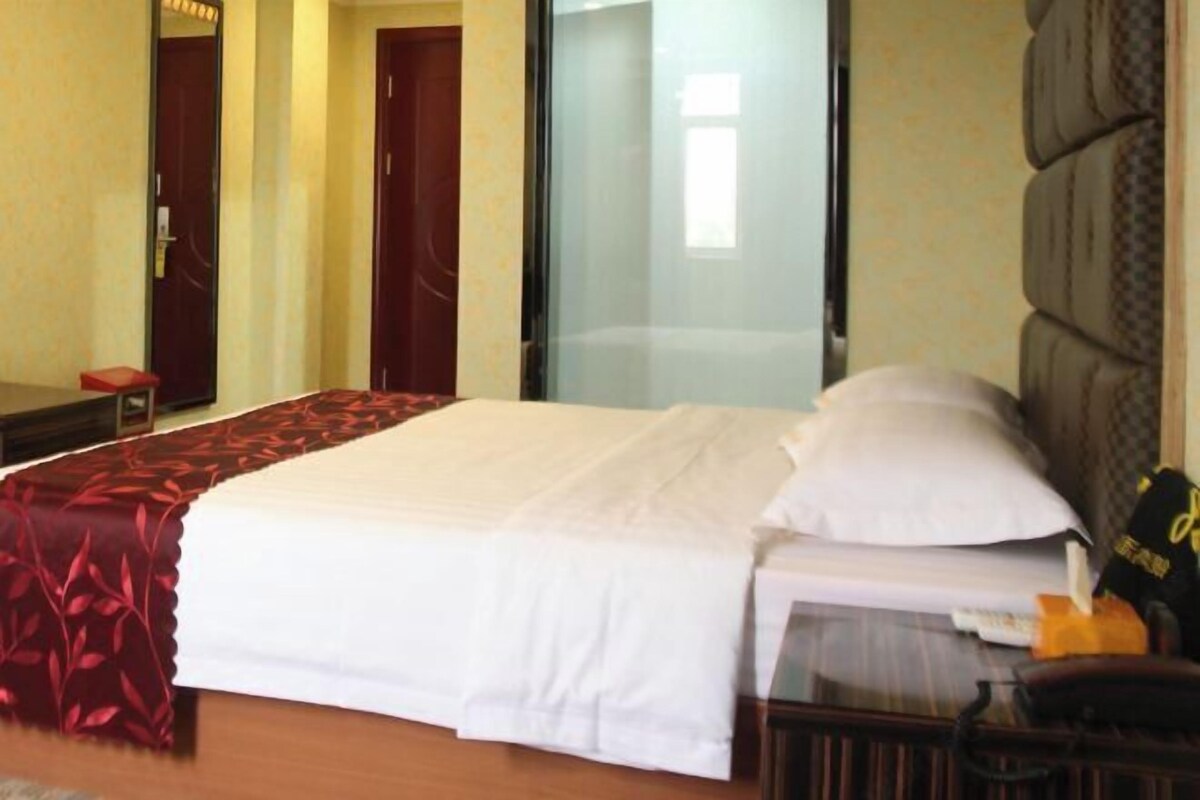 A hotel room with a large bed, a bedside table, a chair, and a glass partition.