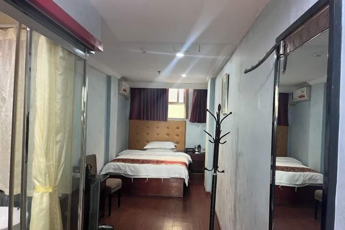 A hotel room with two beds, a mirror, a coat rack, and a window with curtains.