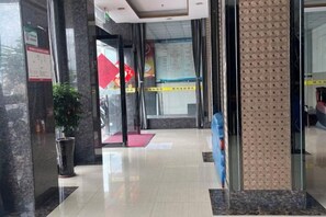 Un vestíbulo de hotel con una recepción, una planta en maceta y una puerta de vidrio que da a otra zona.