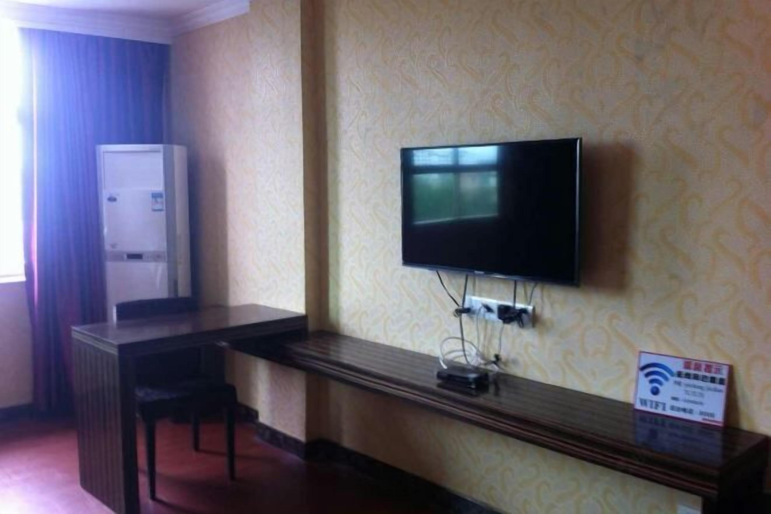 Une chambre d’hôtel équipée d’un téléviseur à écran plat fixé au mur, d’une petite table avec une chaise et d’un réfrigérateur placé dans un coin.