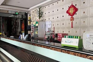 A hotel reception area with a counter, a plant, and a decorative wall. - Yinhong Hostel (Kaiping)