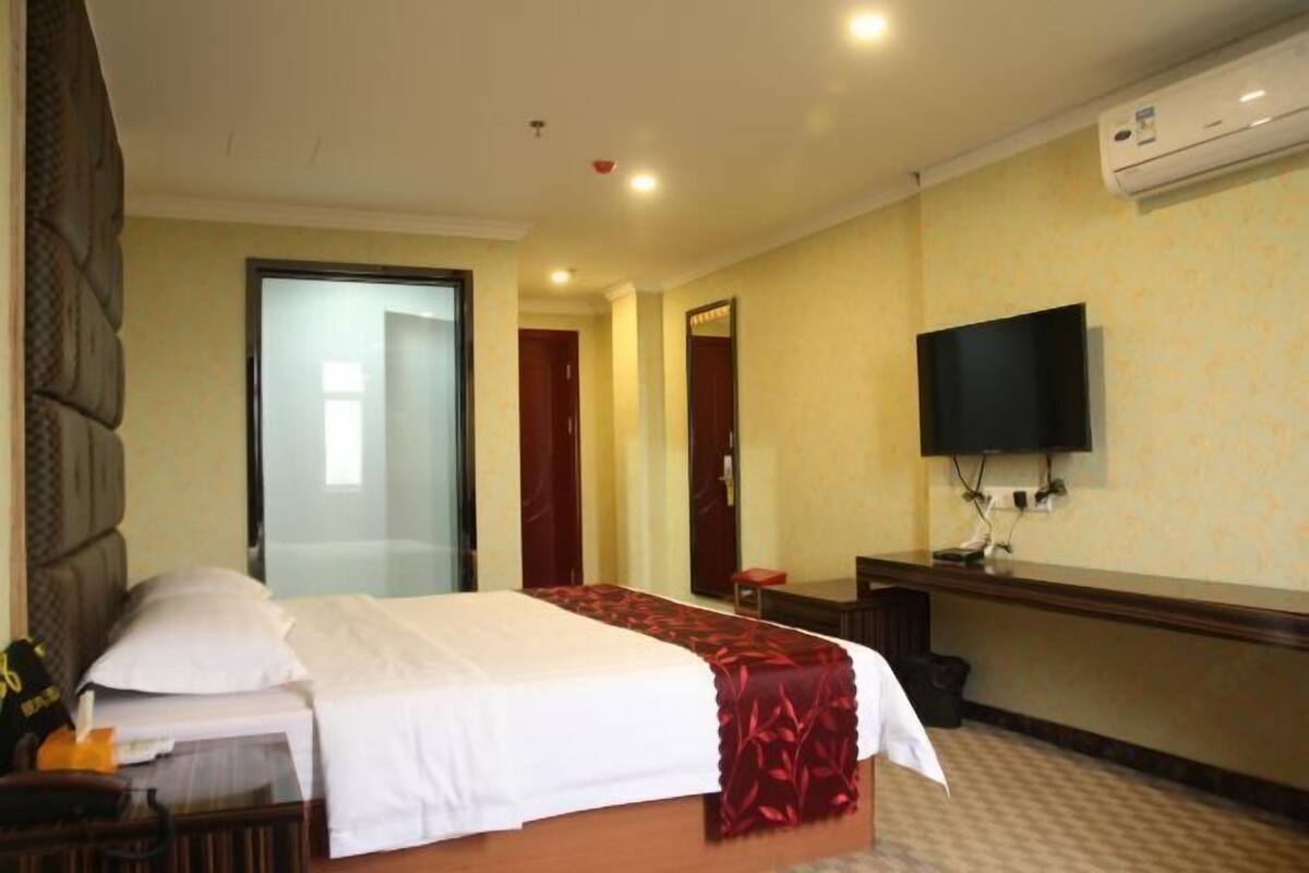 A hotel room with a bed, a desk, a chair, a television, and an air conditioning unit.