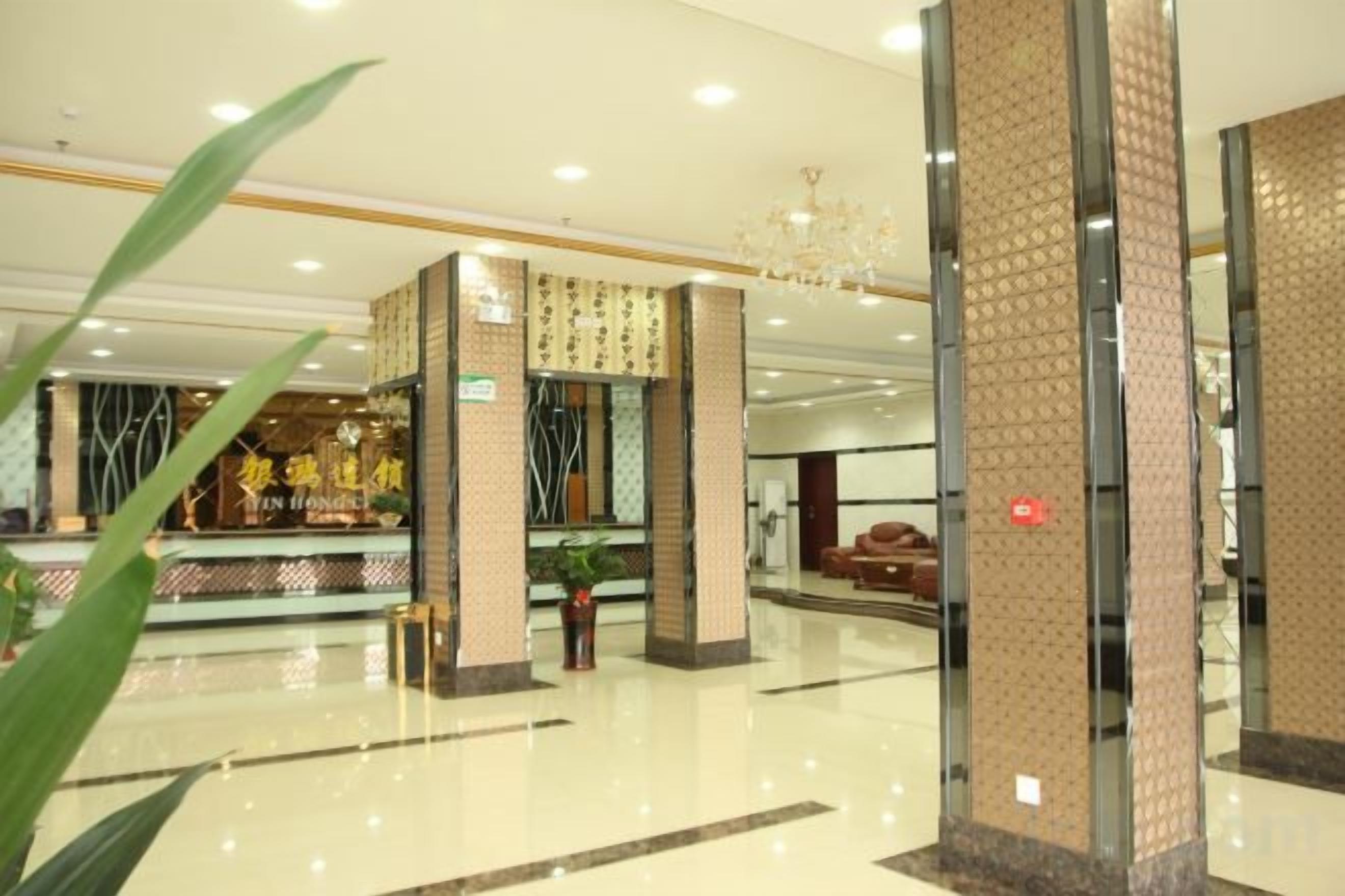 A hotel lobby with a reception desk, a chandelier, and a large plant.
