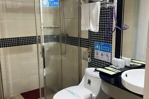 A bathroom with a glass-enclosed shower, a white toilet, and a sink with a mirror above it. There are towels hanging on the wall and a sign with symbols indicating facilities. - Yinhong Hostel (Kaiping)