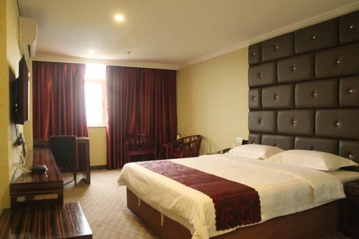 A hotel room with a large bed, a desk, a chair, and a television.