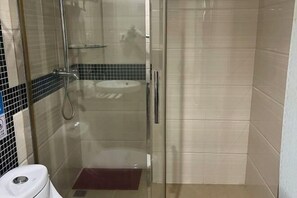 Ein kleines, separates Badezimmer mit Glastür, Waschbecken und Duschbereich.