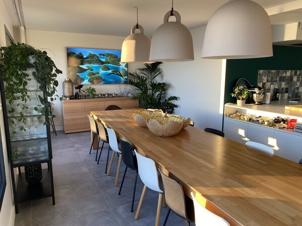 A modern dining area with a wooden table, white chairs, pendant lights, and a large painting on the wall.