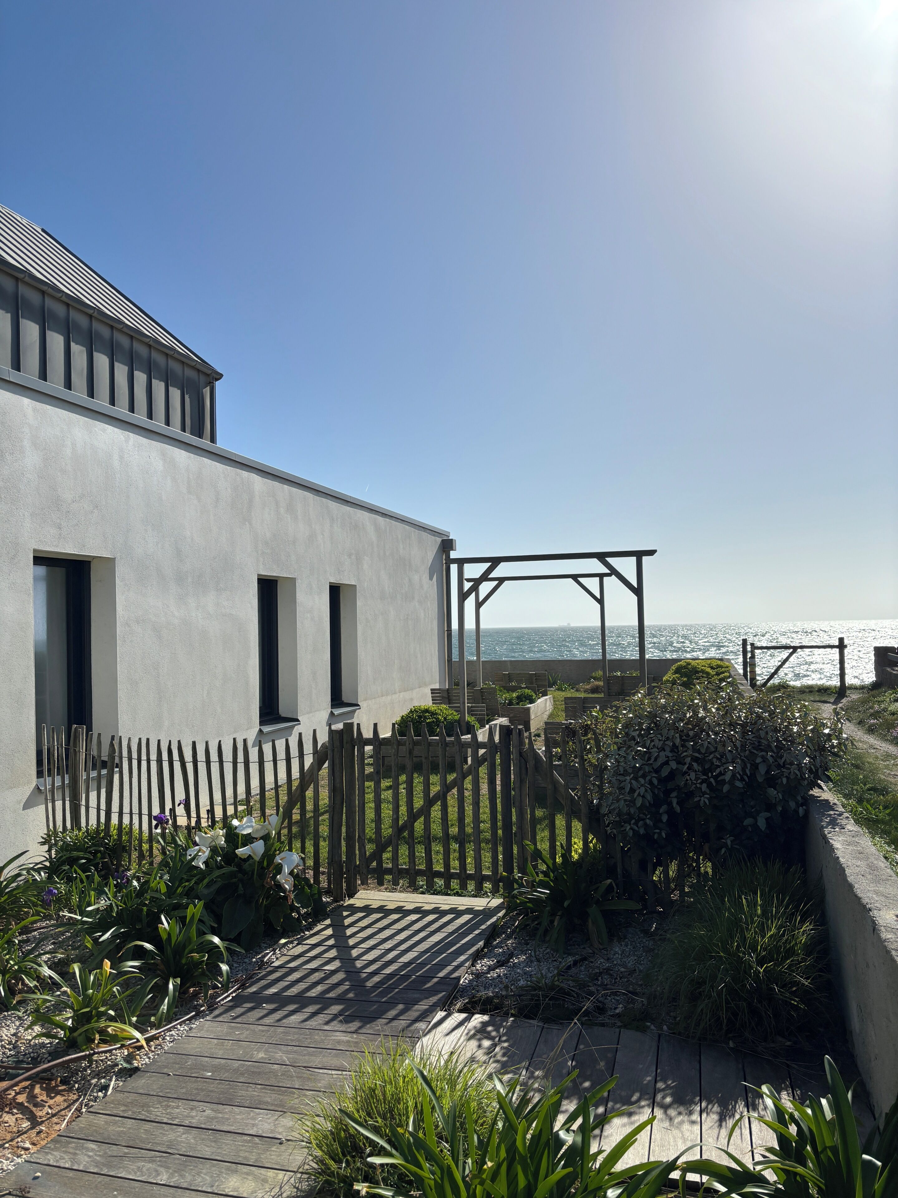 Een modern gebouw met een houten terras, een metalen poort en uitzicht op de oceaan.