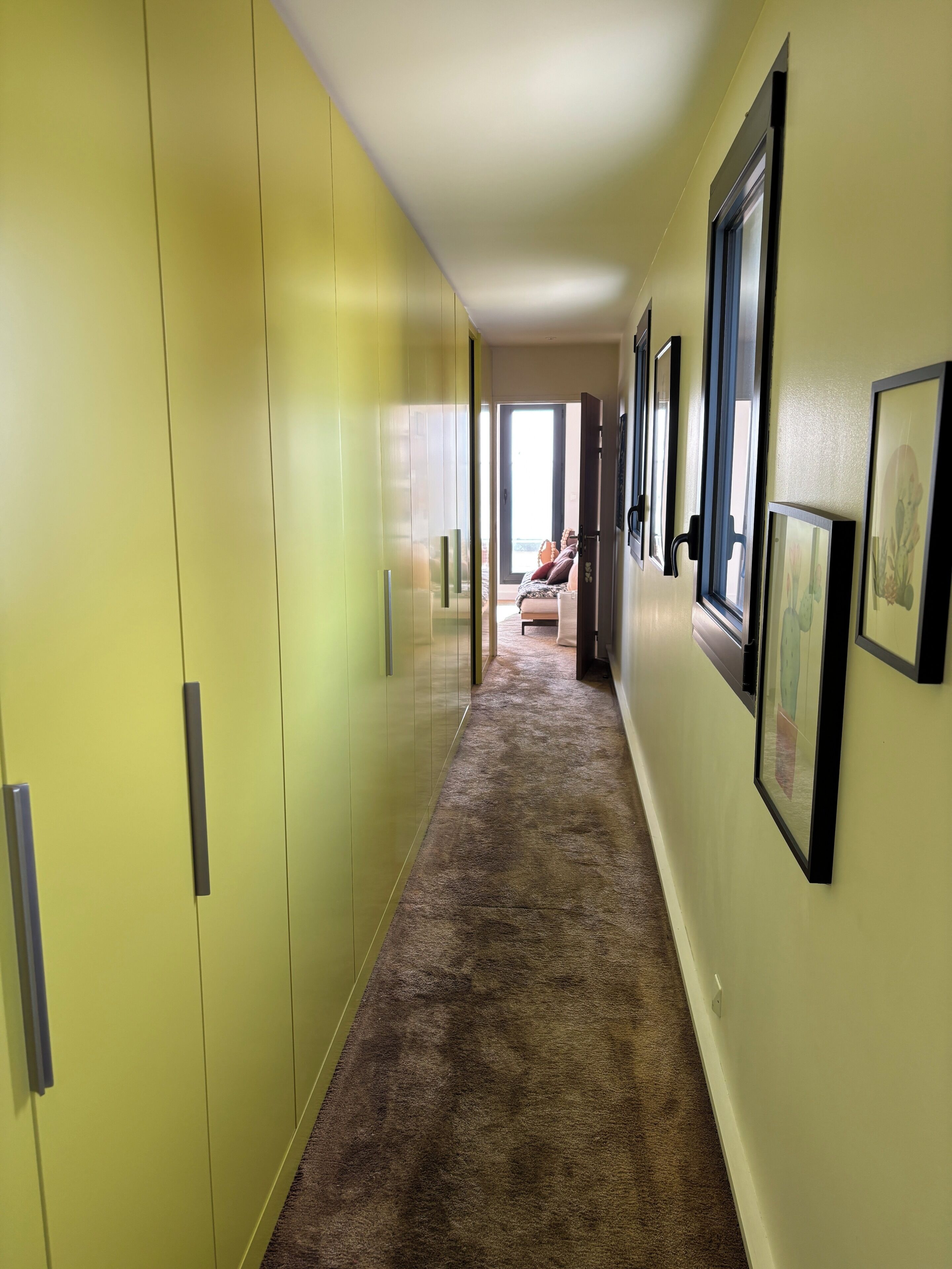 A hallway with a carpeted floor, yellow walls, and framed pictures on the walls.