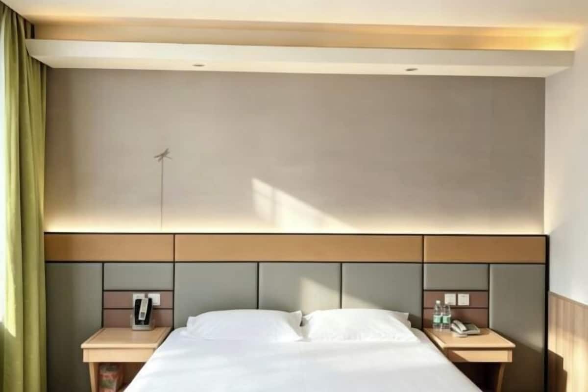 Habitación de hotel con una cama, dos mesitas de noche, un teléfono en la pared y un escritorio pequeño con una silla.