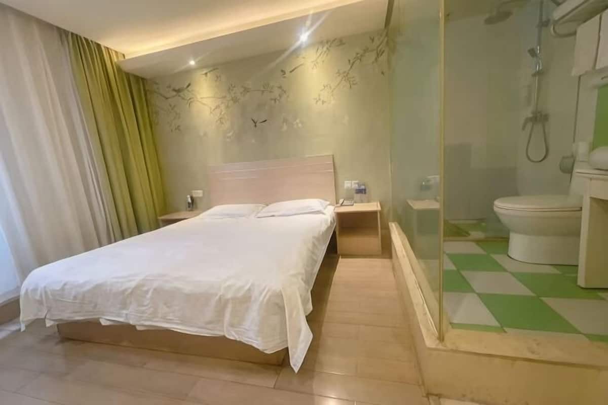 Una habitación de hotel con cama, mesita de noche y baño con inodoro y ducha.