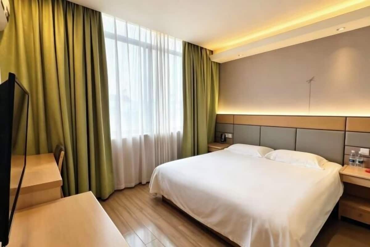 Habitación de hotel con cama, escritorio, silla, televisor y cortinas.