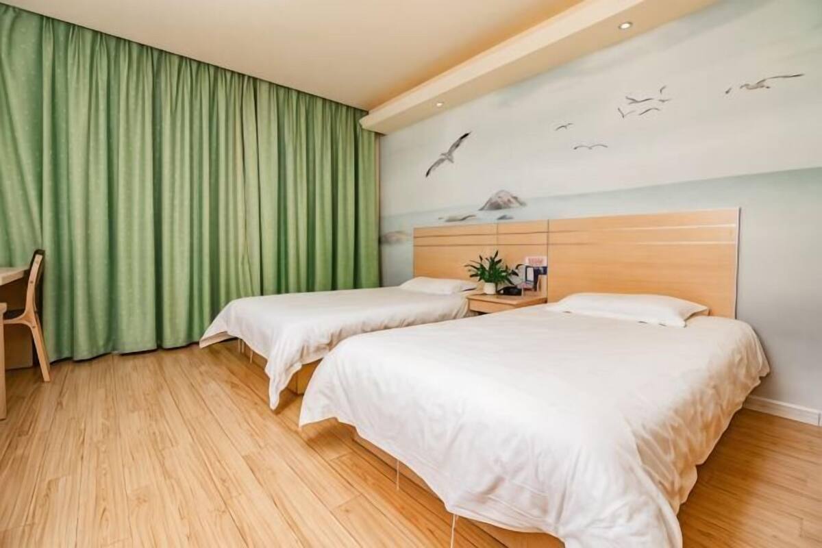 Una habitación de hotel con dos camas, un escritorio, una silla y una cortina verde.