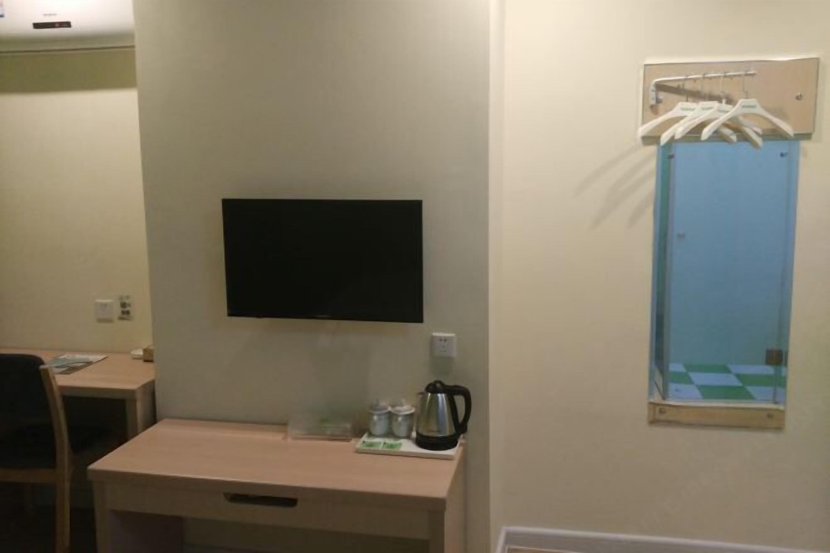 A hotel room with a desk, a television, a mirror, and a small window with a checkered view.