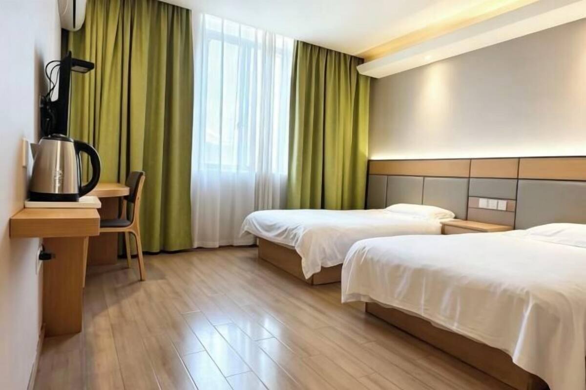 Habitación de hotel con dos camas, un escritorio con tetera y una silla.