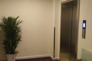 Um elevador com painel de controle, um vaso de planta e uma luminária fixada na parede.