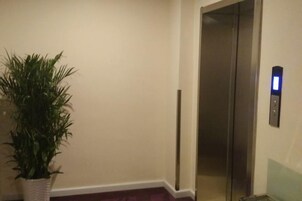An elevator with a control panel, a potted plant, and a wall-mounted light fixture.
