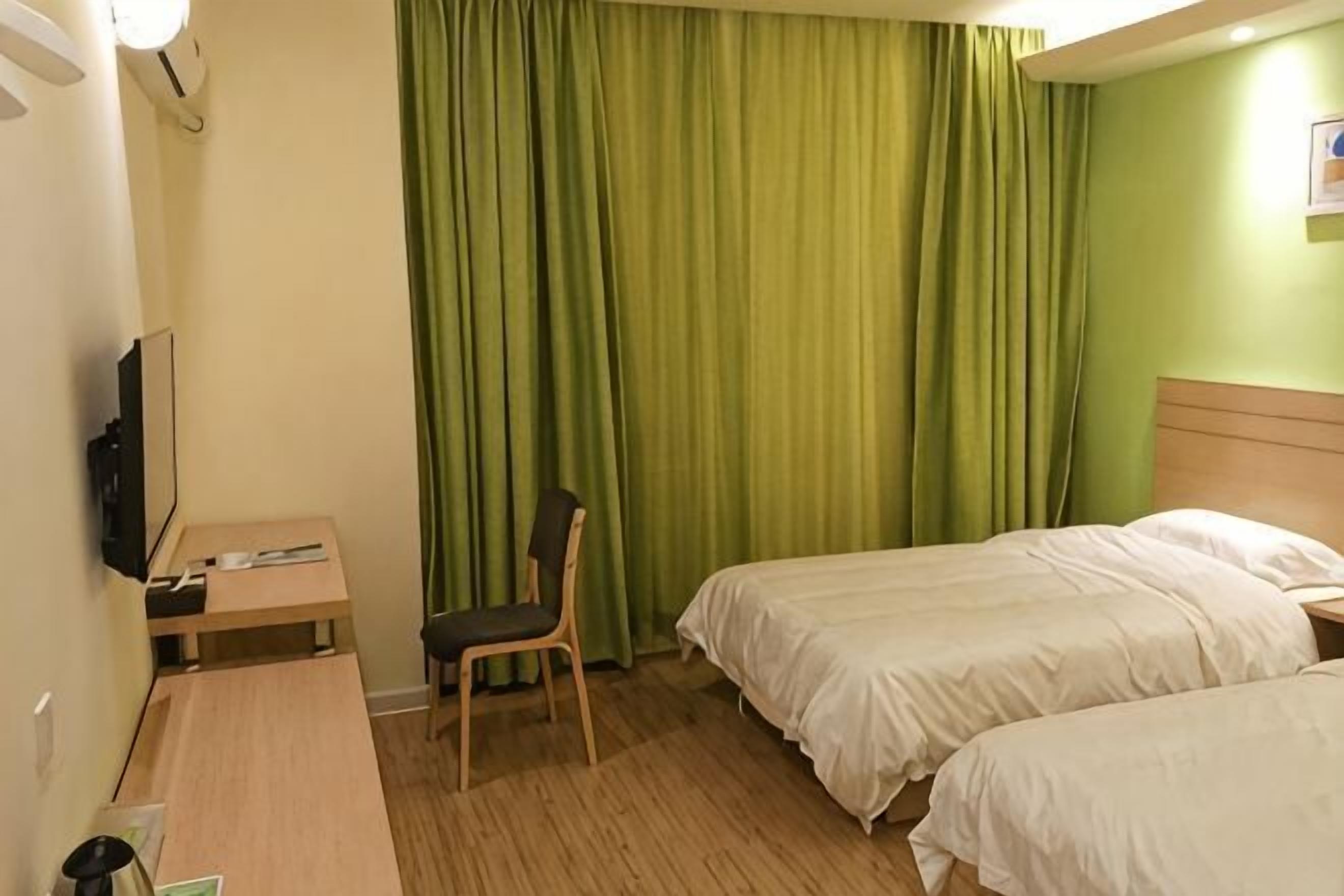 A hotel room with two beds, a desk, a chair, a TV, and green curtains.
