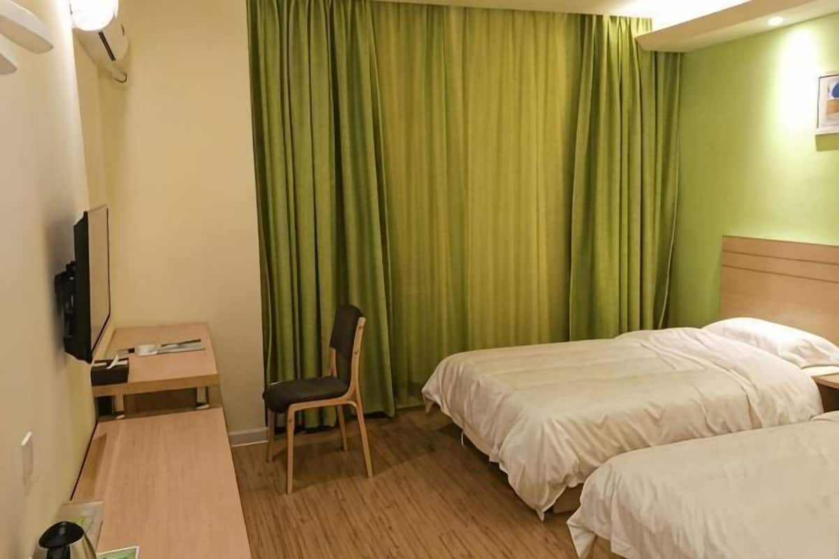 Habitación de hotel con dos camas, un escritorio, una silla, un televisor y cortinas verdes.