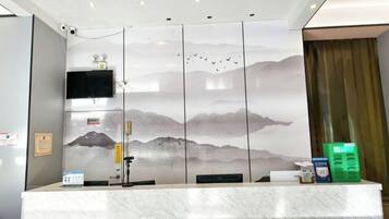 A reception desk with a view of mountains through a patterned wall, a flat-screen TV, and a security camera.