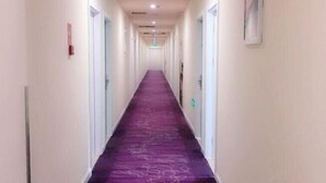 Un largo pasillo con alfombra morada y paredes blancas.