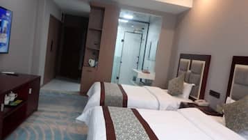 A hotel room with two beds, a desk, a television, and a bathroom visible through a glass door.