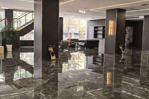 A spacious lobby with a polished marble floor, a staircase, and seating areas.