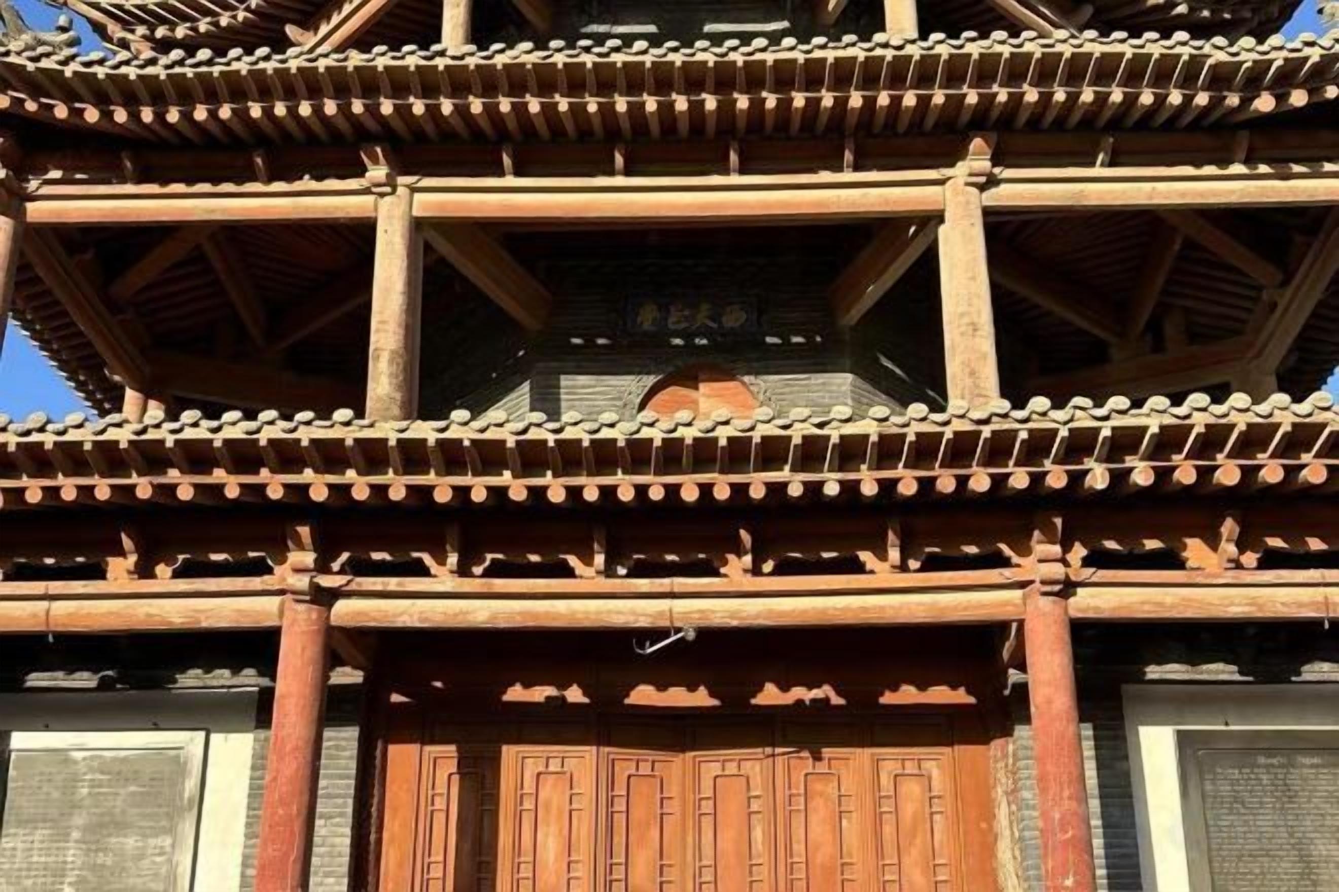 Una estructura de madera tradicional con varios niveles, techo de tejas y una puerta grande de madera.