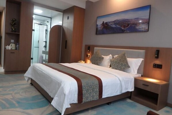 Hotelkamer met een groot bed, nachtkastje, wandtelevisie en een badkamer zichtbaar door een geopende deur.