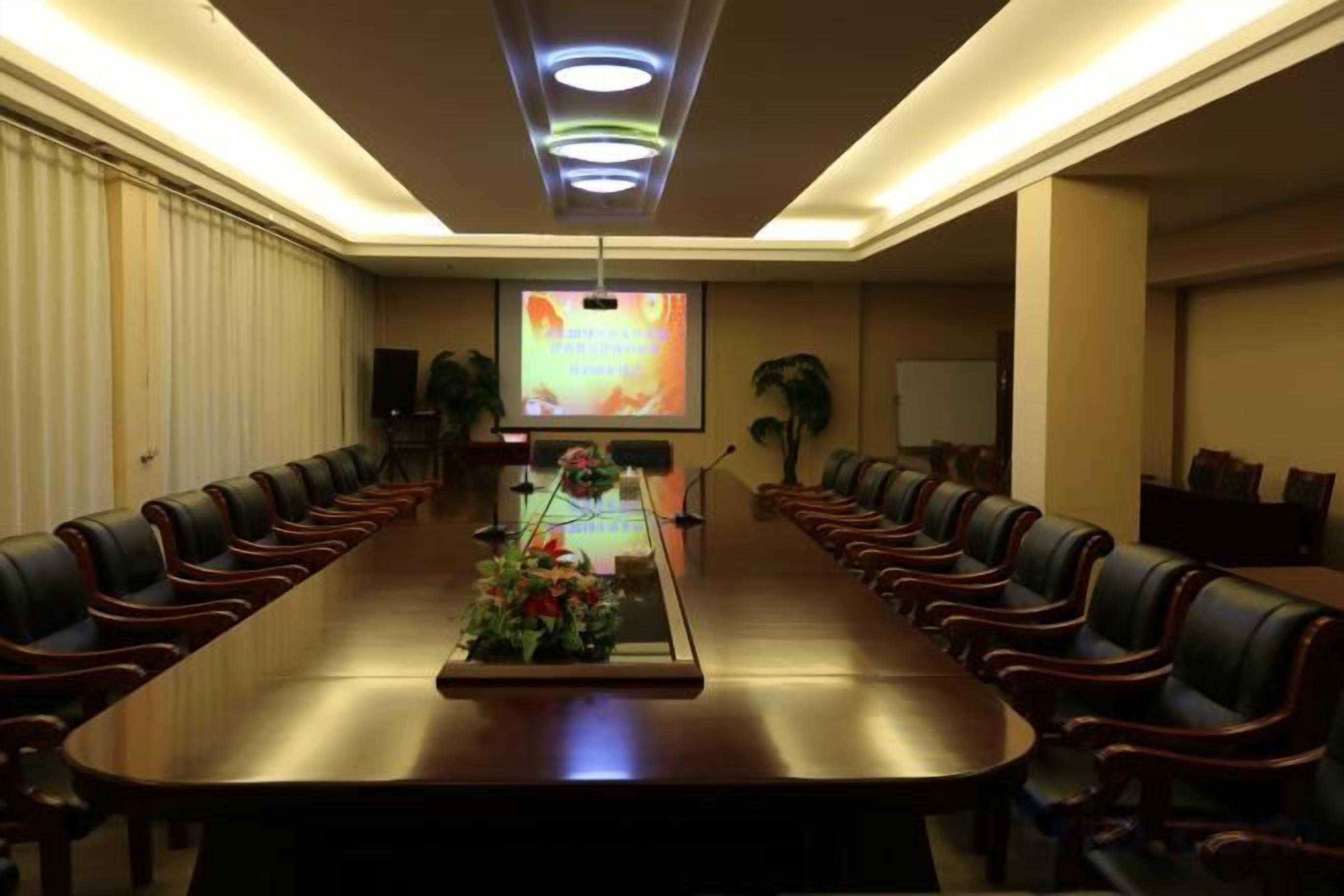 A conference room with a long table, chairs, a projector screen, and a floral centerpiece.