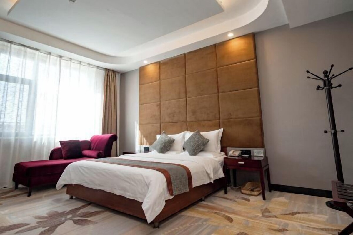 Een hotelkamer met een groot bed, een nachtkastje, een kapstok en uitzicht op de stad door het raam.