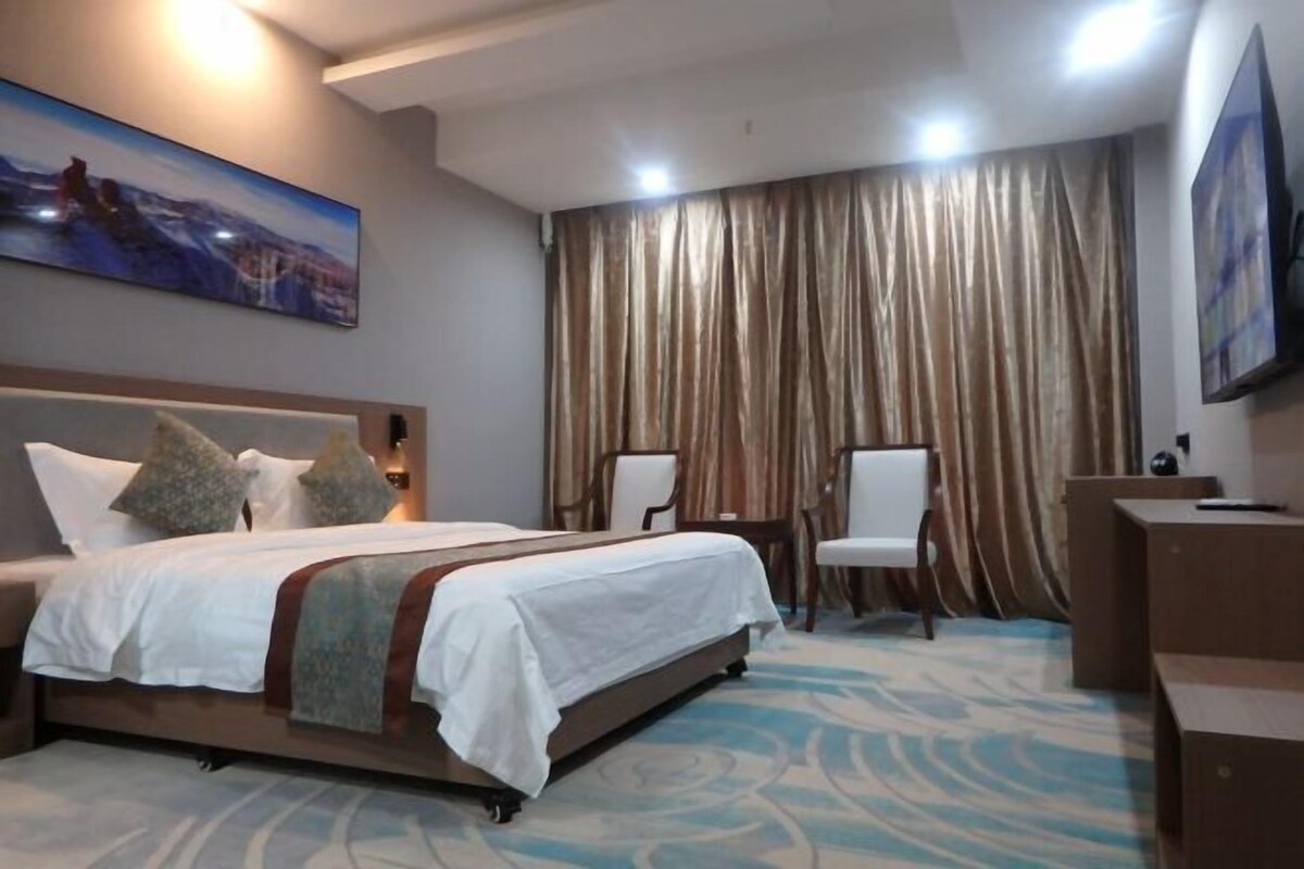 Een hotelkamer met een bed, een bureau, een stoel, een televisie en een schilderij aan de muur.