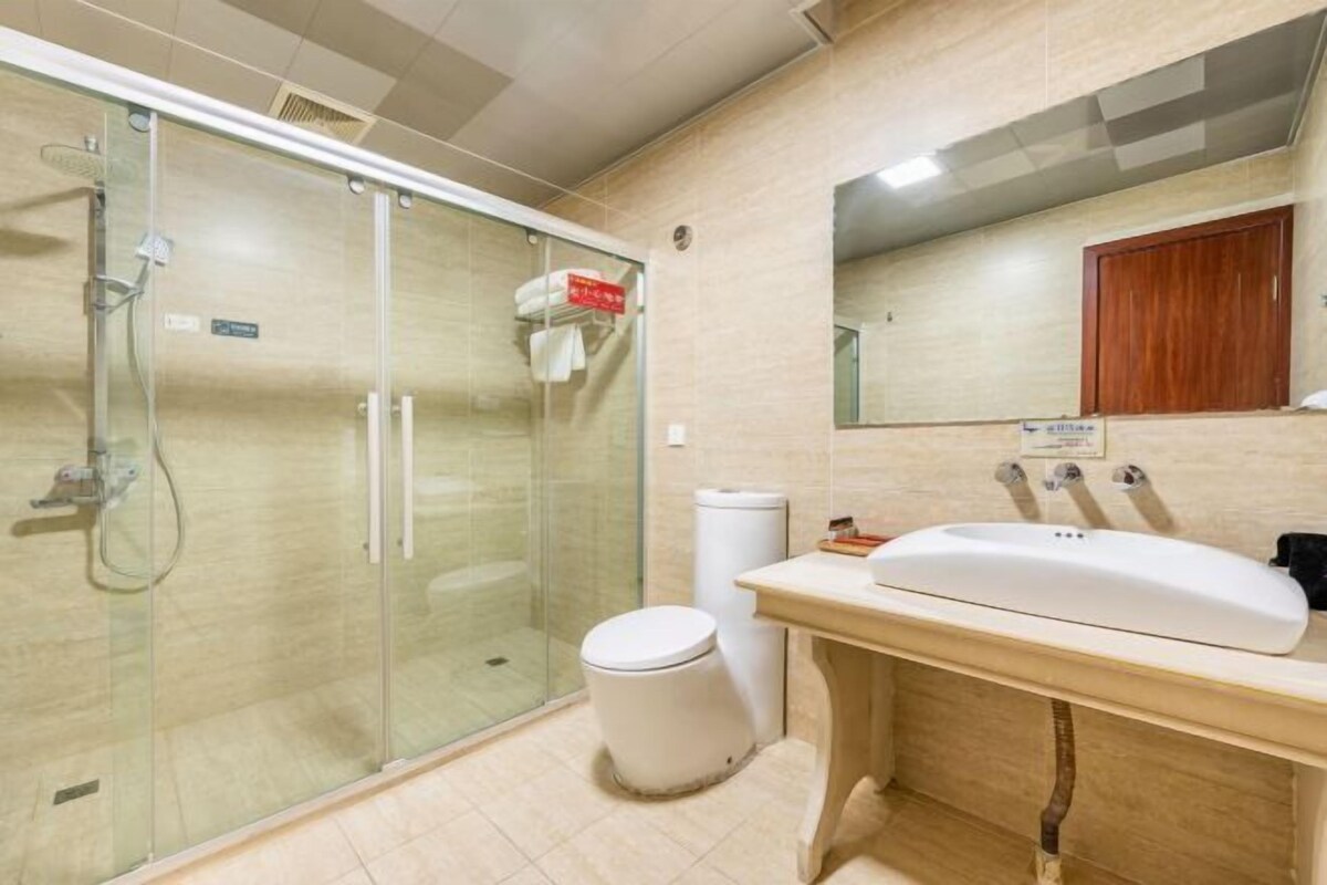 Een badkamer met een douchecabine van glas, een wit toilet, een wastafel met een spiegel erboven en een houten kastje eronder.