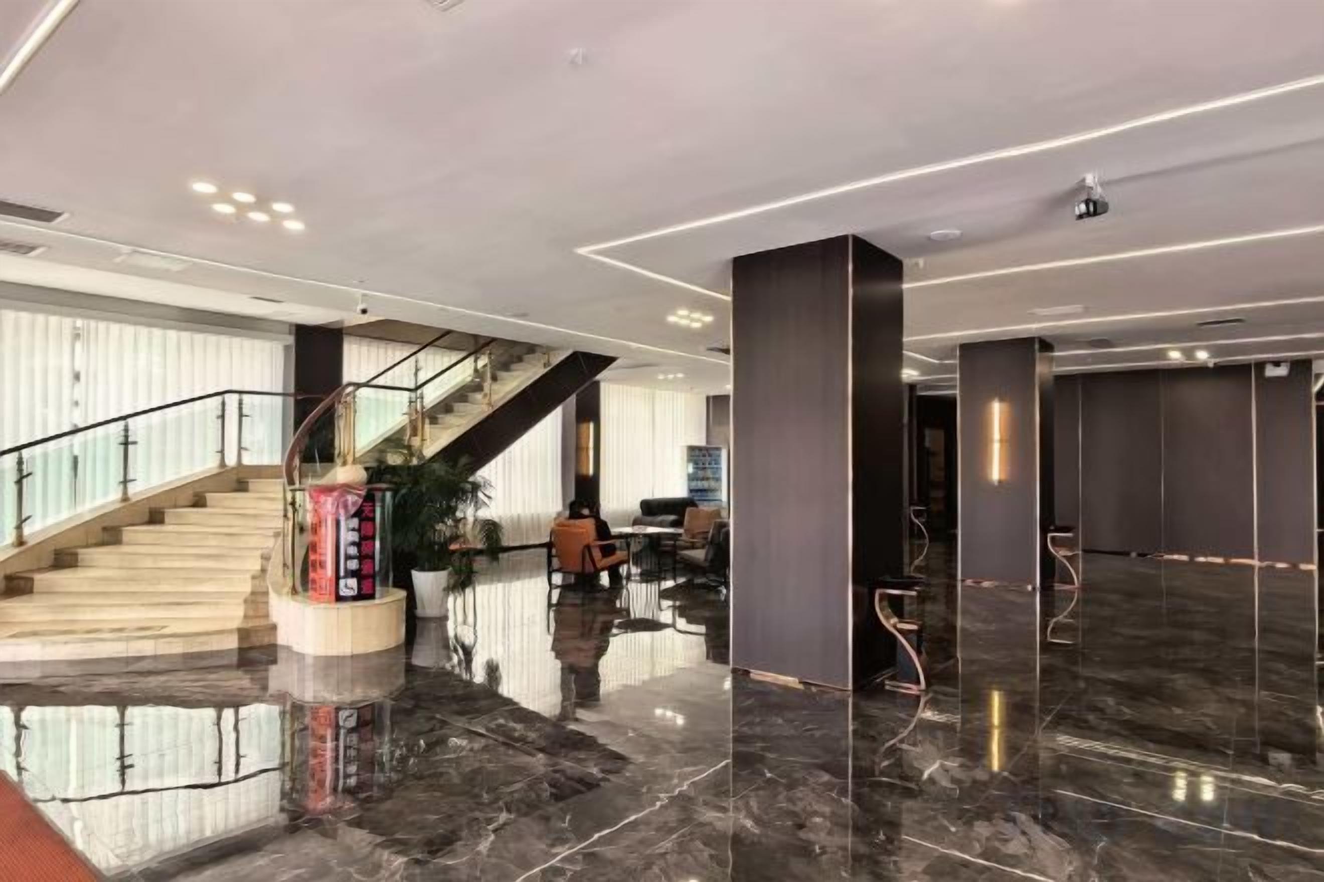 A hotel lobby with a marble floor, a staircase, and a reception desk.